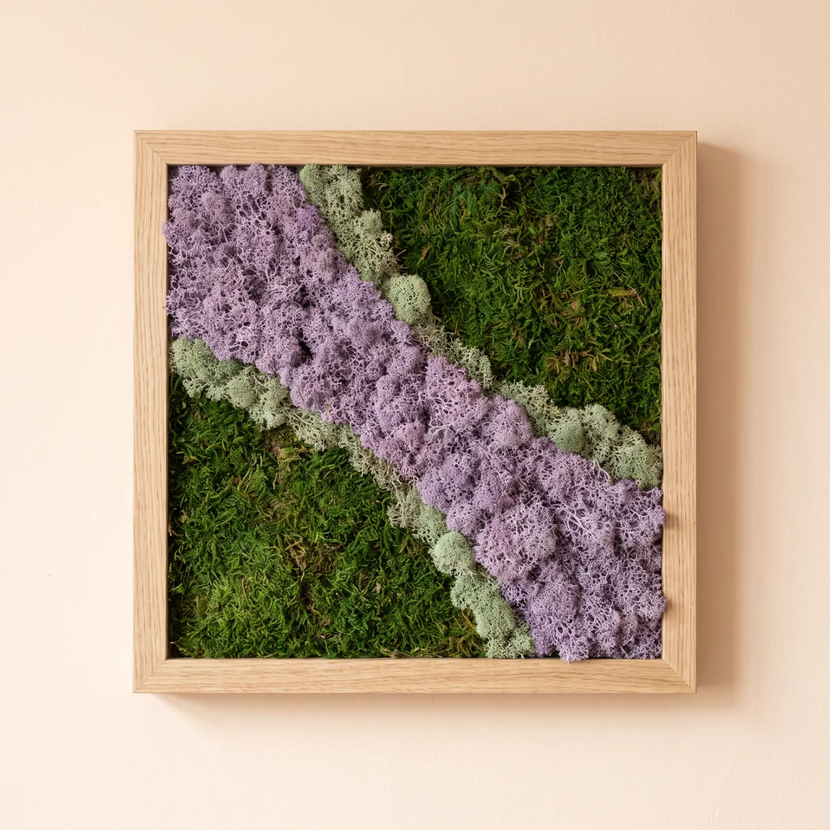 Una composición en tonos lilas con texturas de musgo y liquen preservados, en un marco cuadrado de roble claro.