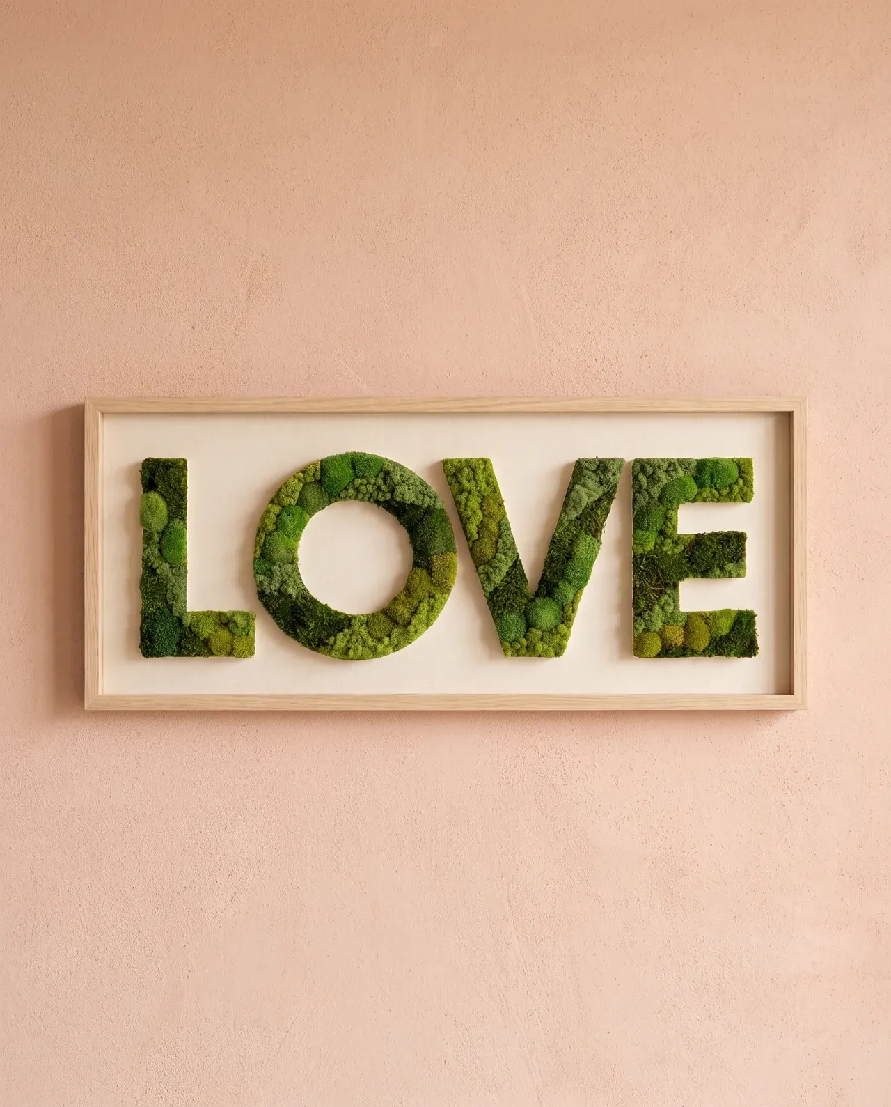 La palabra LOVE, cubierta de musgos de distintas texturas, destaca sobre un fondo marfil dentro de un marco horizontal de roble.
