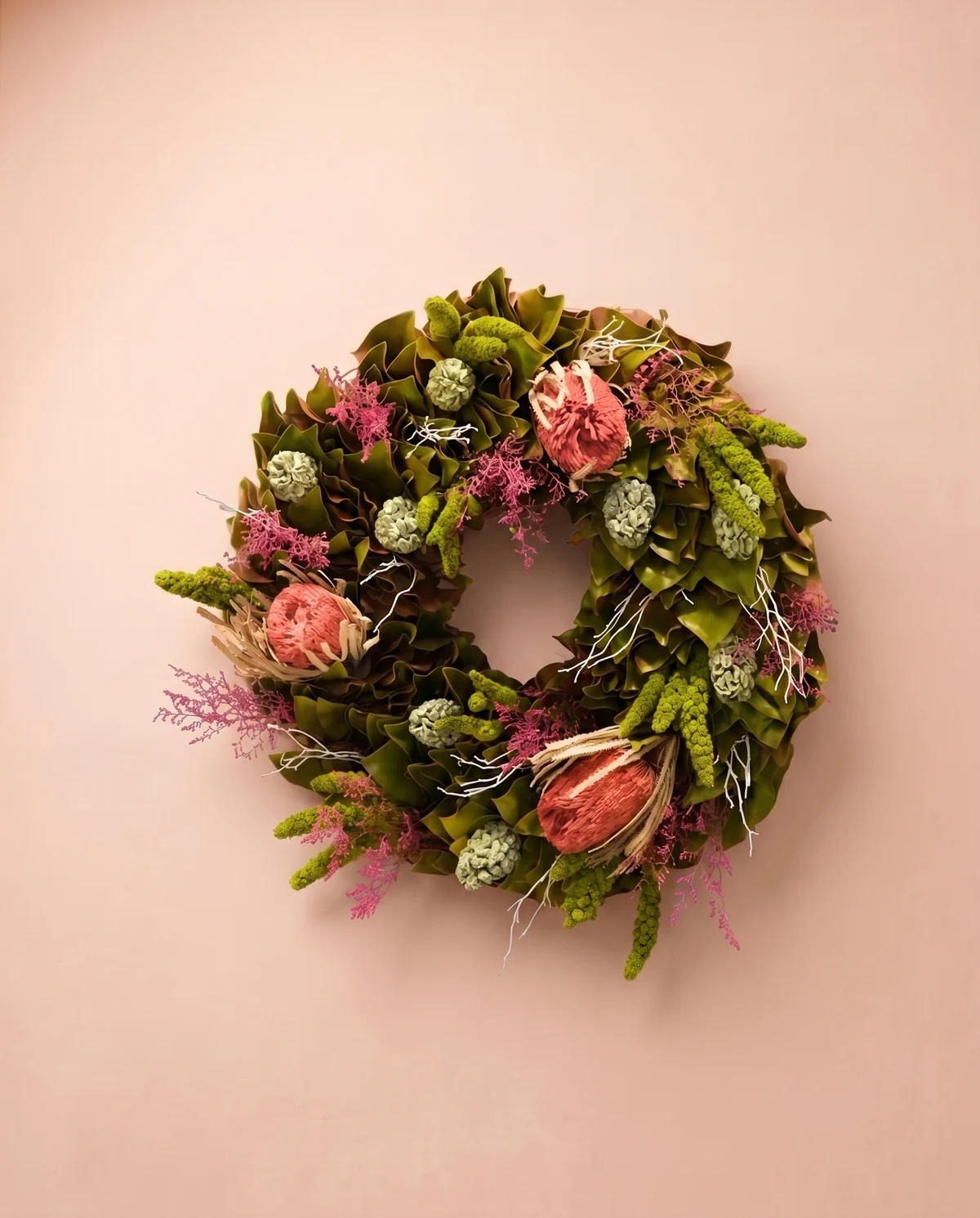 Follaje y flores preservadas se agrupan en una corona de verdes y acentos rosados.
