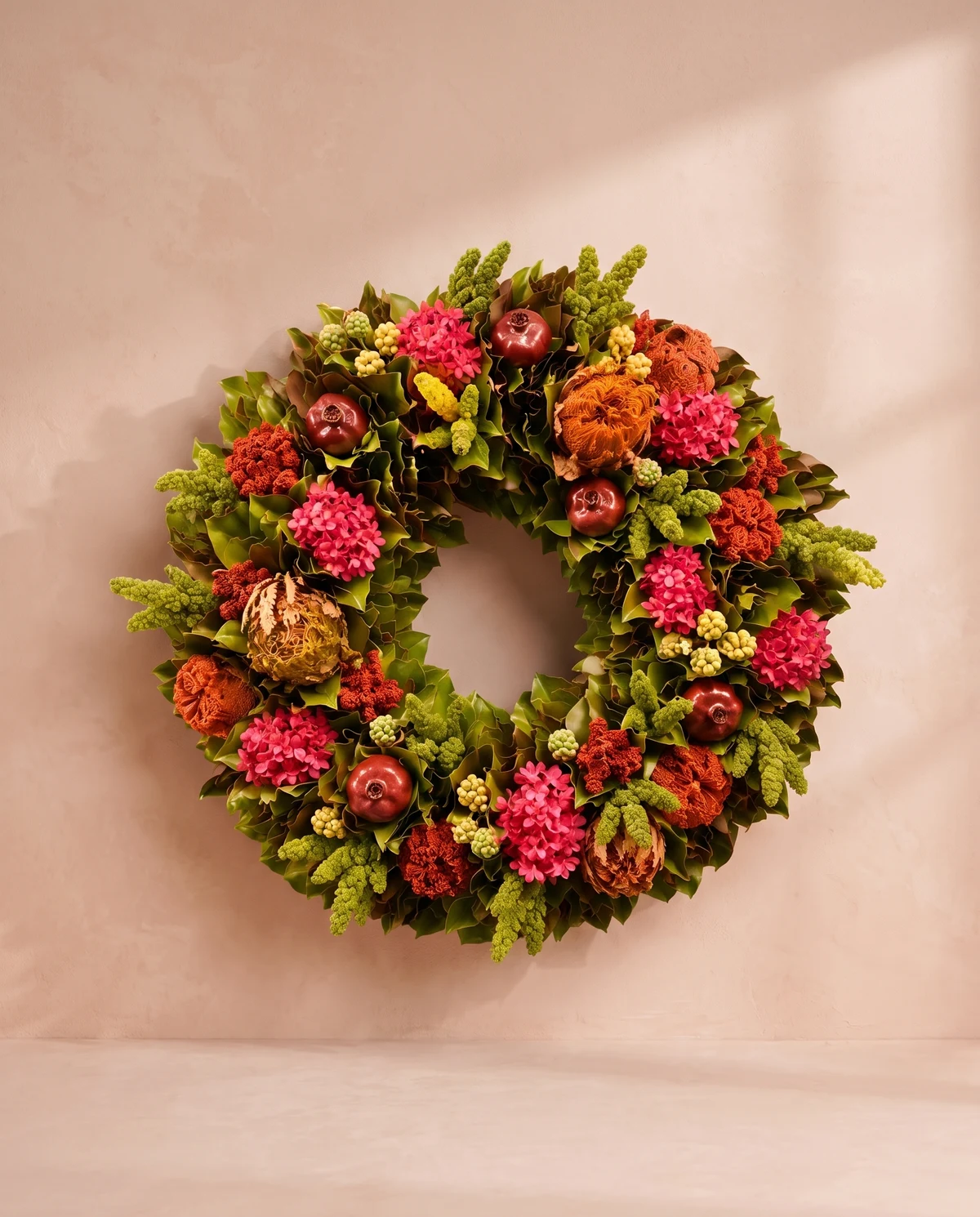Una corona de follaje verde y flores preservadas en tonos cálidos y vivos.